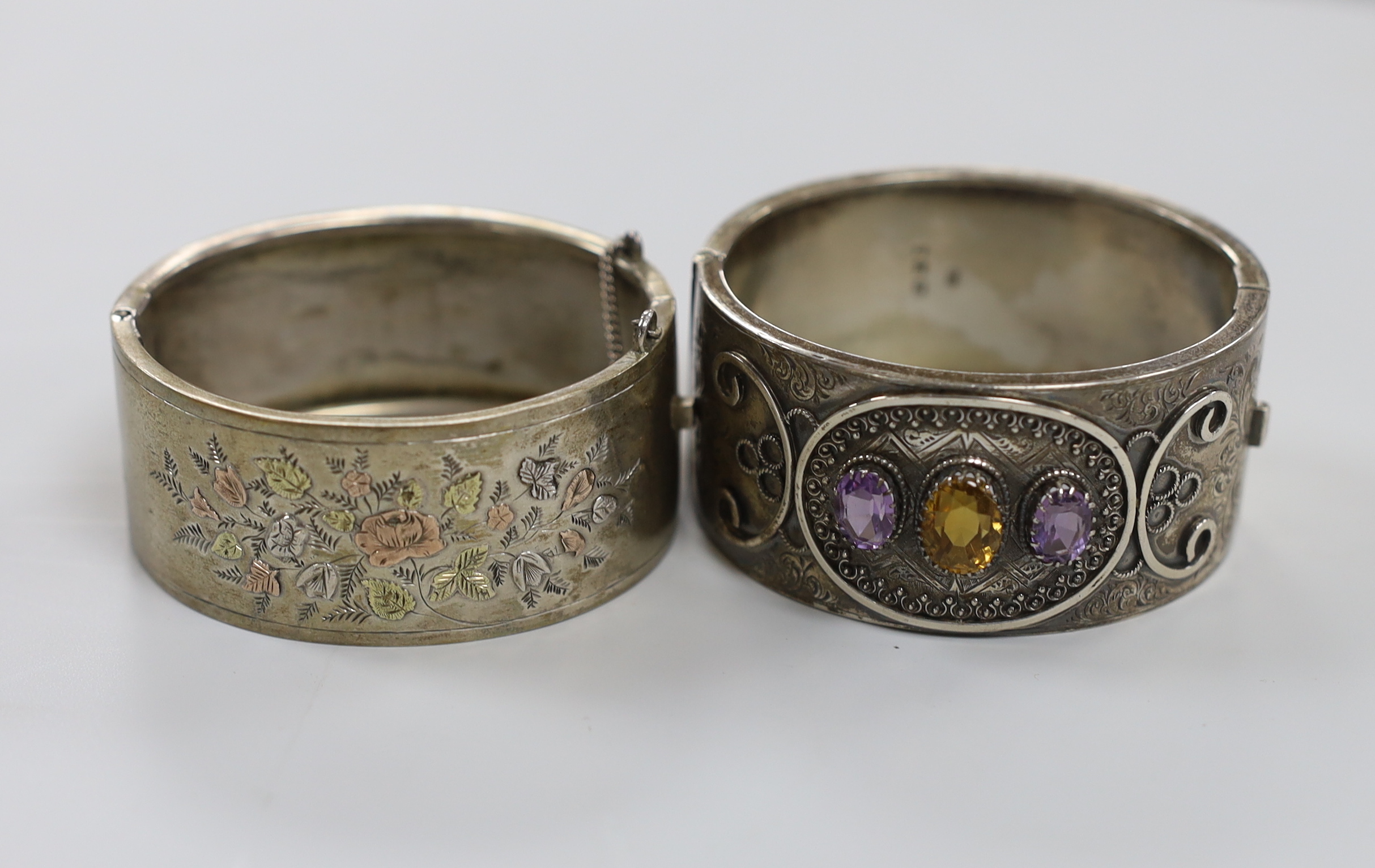 A late Victorian silver and three stone amethyst and citrine set hinged bangle and a later white metal bangle.